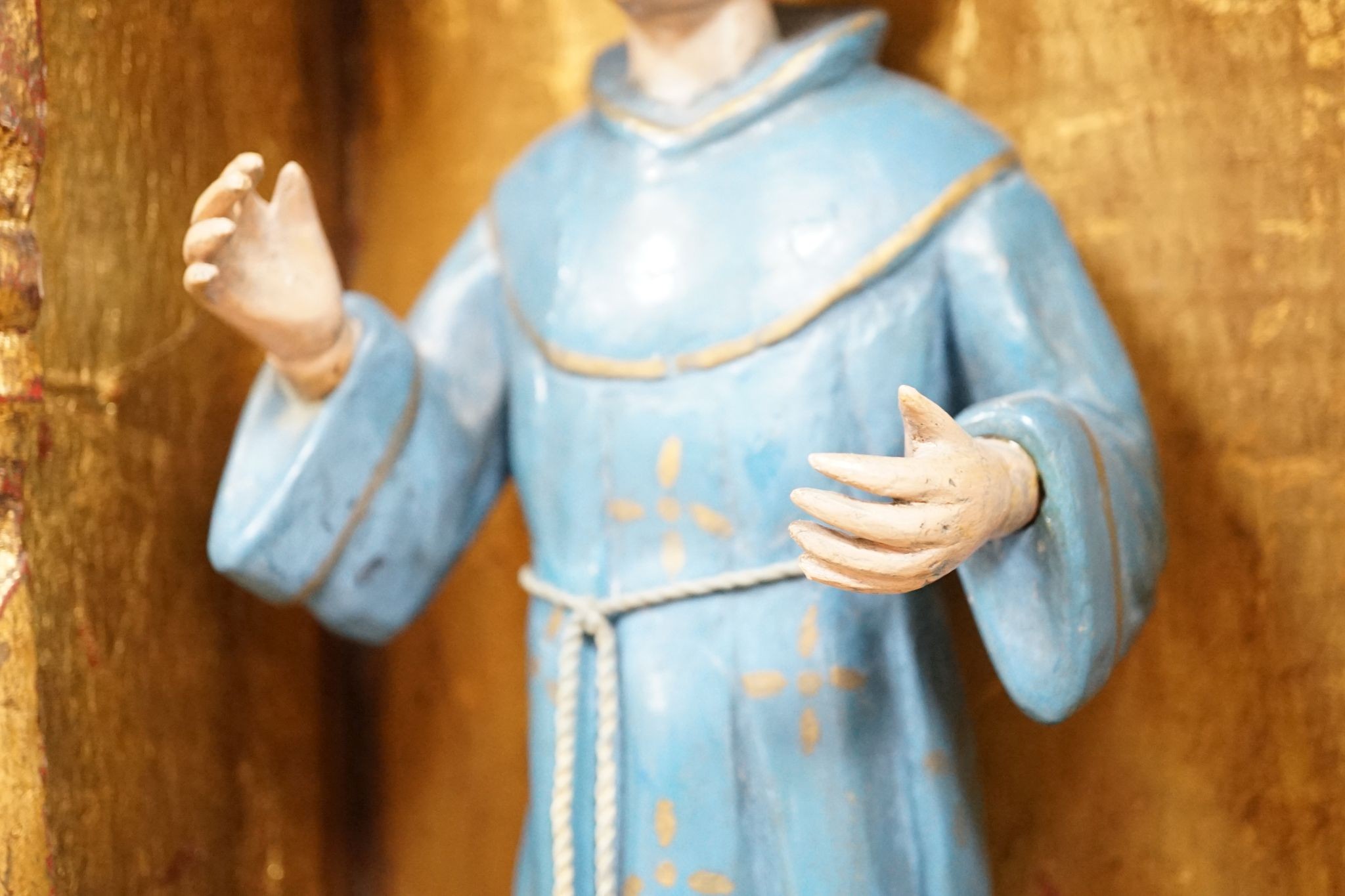 A painted saint with a blue robe and gilt metal halo, standing in an ornate carved niche, 57cm